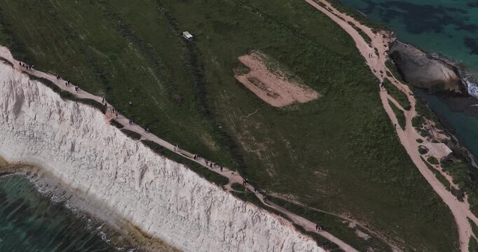 Aerial view of the winding dirt trails bisecting the lush green landscape, contrasting sharply with the white cliffs and turquoise waters, Munxar Path, Marsaskala, Malta.