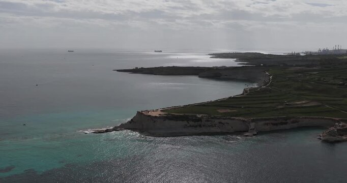 Aerial view of the rugged coastline, where turquoise waters meet dramatic cliffs and lush green fields, creating a stunning contrast of colors, Munxar Path, Marsaskala, Malta.