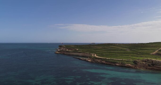 Aerial view of the Munxar Path coastline with terraced fields meeting the turquoise sea, creating a stunning contrast of green and blue, Marsaskala, Malta.