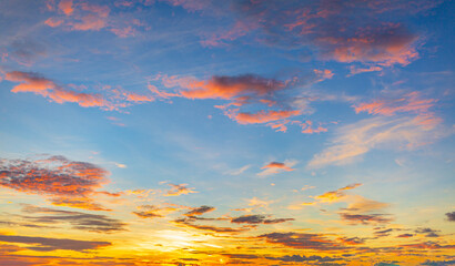 Obraz premium Dramatic sunset sky with orange and blue gradient clouds background,A beautiful panoramic view of the twilight sky during sunset, featuring soft wispy clouds illuminated by golden light against.