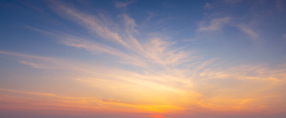 Fototapeta premium Dramatic sunset sky with orange and blue gradient clouds background,A beautiful panoramic view of the twilight sky during sunset, featuring soft wispy clouds illuminated by golden light against.