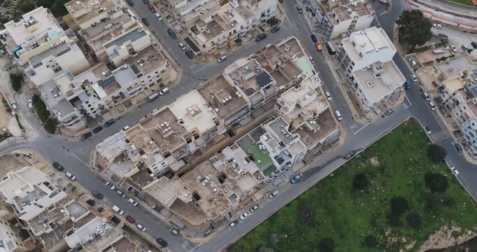 Aerial view of tightly packed buildings and roads, showcasing the urban landscape with green areas surrounding it, Mellieha, Malta.