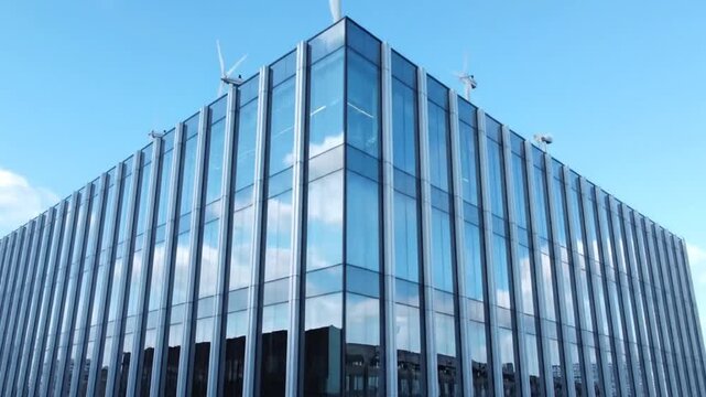 The video captures a modern glass office building's corner against a blue sky. Over eight seconds, small wind turbines progressively appear and spin up along the rooftop, highlighting the structure's