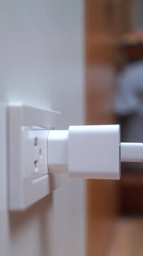 Close up of woman a hand connecting a white power adapter to a wall socket. Concept of charging devices and electricity consumption. Vertical Shot.