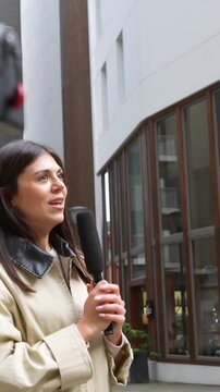 Professional female reporter holding a microphone while conducting a vox pop interview with a young man on a city street, discussing current events for a news broadcast or social media content