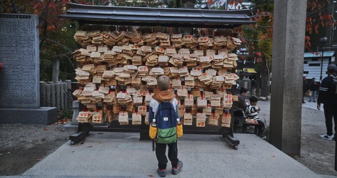 Little boy standing in front of wood objects on wall at shrine