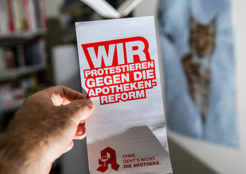 Paris, France - Sep 9, 2025: A hand holds a German leaflet with bold red text protesting the pharmacy reform, displayed indoors with shelves and a blurred lynx poster in the background