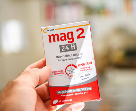 Paris, France - Sep 9, 2025: A hand holds a Mag 2 24H magnesium supplement box showing its red and white design, prolonged release claim and French text in a softly blurred indoor scene