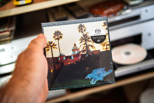 Paris, France - Sep 9, 2025: Hand holding a sealed Hotel California Eagles SACD in an audiophile setup with the iconic cover art visible near an open disc player in a warm home listening space