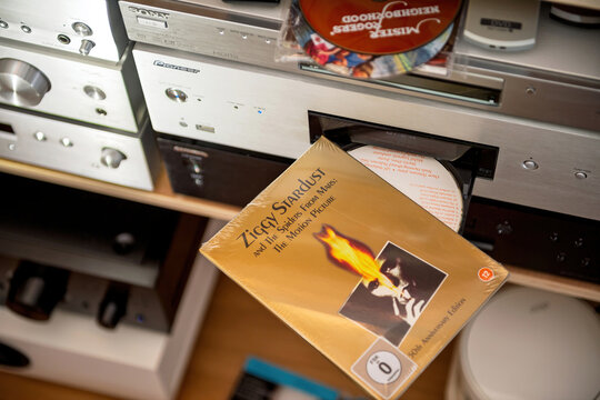 Paris, France - Sep 9, 2025: A hand holds the sealed Ziggy Stardust and the Spiders from Mars motion picture DVD near an open disc tray in a home audio setup with silver hi-fi components