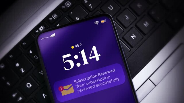 Smartphone displaying subscription renewal alert with time and temperature on laptop keyboard for tech concept, 4k footage