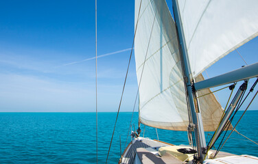 Landscape view from bow of luxury sailing boat yacht with detail of main mast and rigging showing blue ocean background