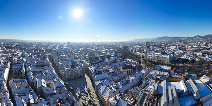 Aerial view of snow-dusted rooftops and streets converge towards the iconic Hauptplatz, a winter panorama bathed in the glow of a bright sun, Graz, Styria, Austria.