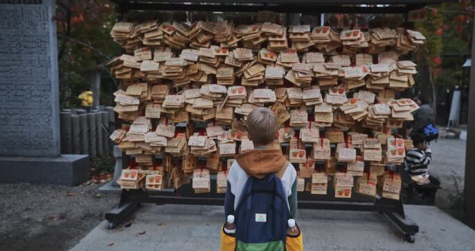 Child walking up to wall of wooden objects at Japanese shrine - steady cam shot