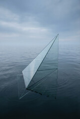 Obraz premium A minimalist glass sculpture floats serenely on calm water under a cloudy sky.
