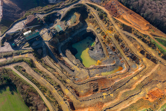 Aerial view of a quarry with tiered earth and a small pool of water reflecting the sky contrasts with the surrounding green fields, La Roche-Jaudy, Brittany, France.