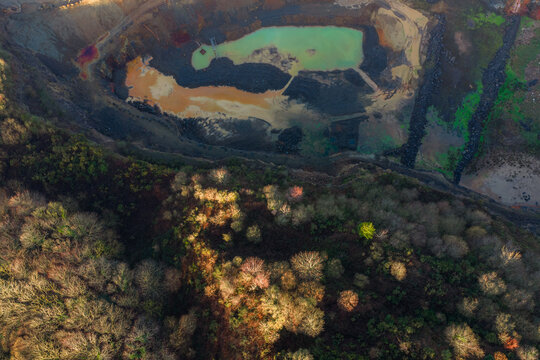 Aerial view of an open pit mine contrasting with the surrounding lush forest, showcasing the stark division between industry and nature, La Roche-Jaudy, Brittany, France.