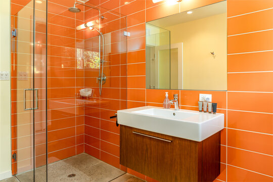 Modern orange tile bathroom interior, walk-in glass shower, sink, cabinet