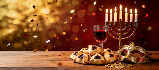 Purim banner with Menorah candles surrounded by hamantaschen cookies, a glass goblet of red wine and a gold mask on a wooden table with space for text. The festive atmosphere of holiday