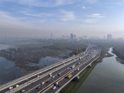 Aerial view of the Vashi Bridge stretching across the Thane Creek, carrying a stream of traffic towards the hazy skyline, Vashi, Maharashtra, India.