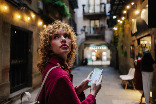 Woman holding searching directions and holding smart phone at alley