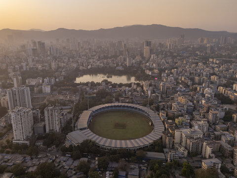 Aerial view of the stadium nestled amidst the sprawling cityscape, with the tranquil lake reflecting the soft light, Thane, Maharashtra, India.