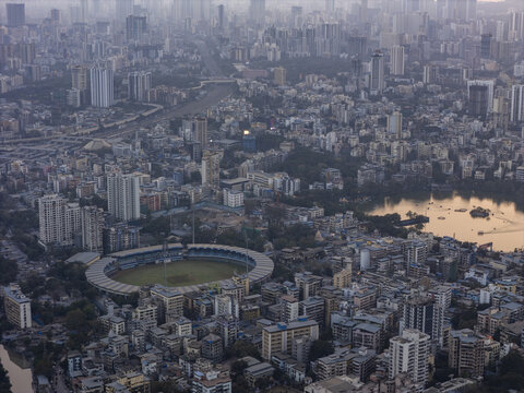 Aerial view of a dense cityscape where modern buildings meet the serene Masunda Lake and the vibrant Dadoji Kondadev Stadium, Thane, Maharashtra, India.