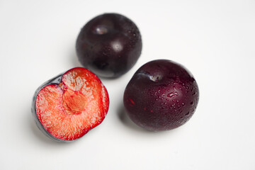Obraz premium Three plums, one of which is cut in half