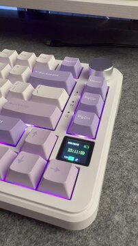 Close up of a white mechanical keyboard featuring a small LCD screen and purple RGB lighting.