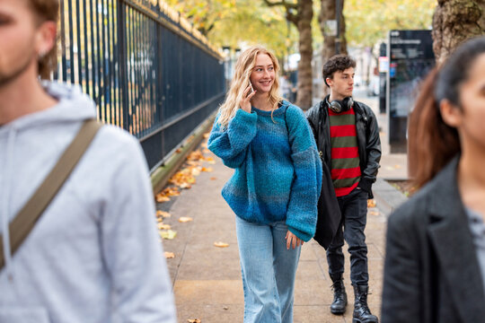 Smiling woman walking on city sidewalk during autumn rush hour