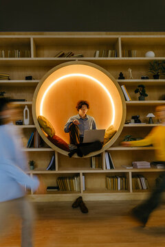 Person relaxing in circular library seat using laptop indoors