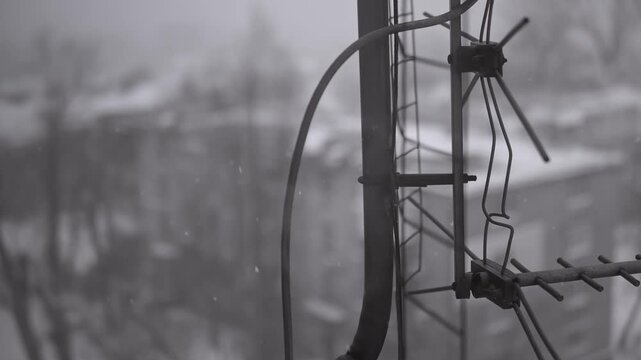 Old television antenna stands outside during a winter snowstorm. Black and white footage creates a gloomy, melancholic, and nostalgic atmosphere.