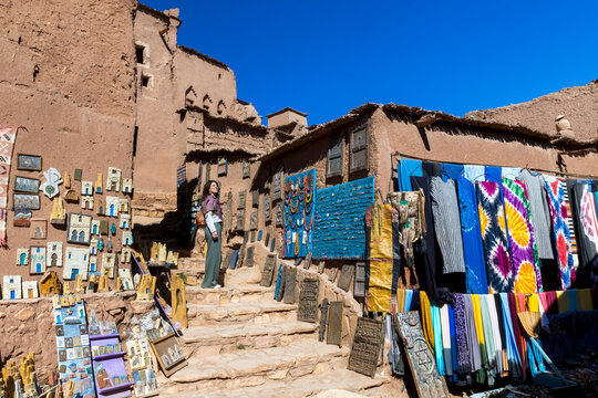 A woman stands on stone steps surrounded by shops selling crafts and clothing in a traditional Moroccan village. Kasbah ait ben haddou,Marrakech,Morocco