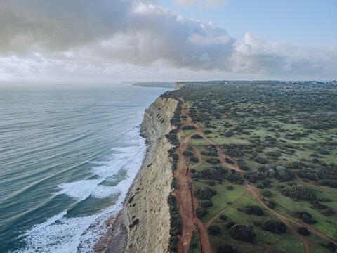 Aerial view of rugged cliffs meet the turquoise sea, contrasting with the lush green landscape, Praia do Porto de Mos, Lagos, Faro, Portugal.