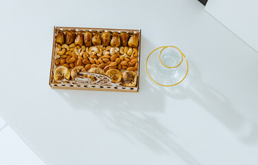 Wooden carved Ramadan tray with various dried fruits and a glass of water on the table.