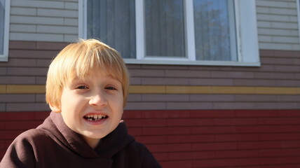 A blond boy of European appearance writing homework at a table in the school yard in the spring