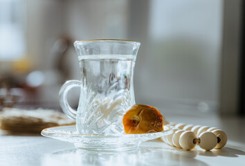 Plain water in a glass of armud, a date and prayer beads on a white kitchen table.
