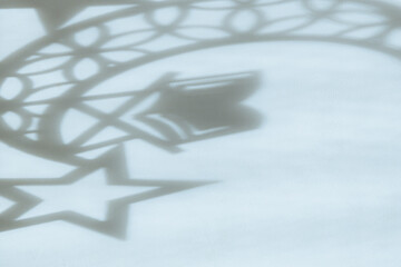 Drawing of a shadow in the form of a star, a crescent moon and a book on a stand on white.