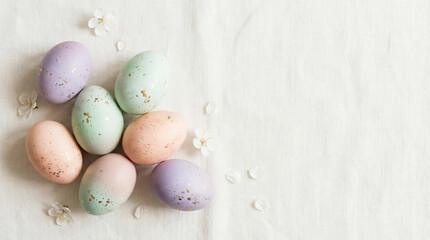 Pastel Easter eggs with gold speckles arranged on white fabric, surrounded by small white blossoms. Festive springtime decoration symbolizing Easter, renewal, and seasonal celebration