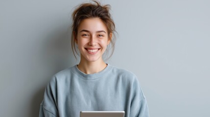 Happy young woman smiling while holding a digital tablet against a grey background.