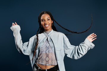 Fashionable young woman with long braids expresses joy in a stylish outfit against a blue backdrop