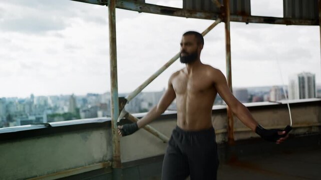 Determined Black male boxer jumping rope on empty rooftop, cardio workout