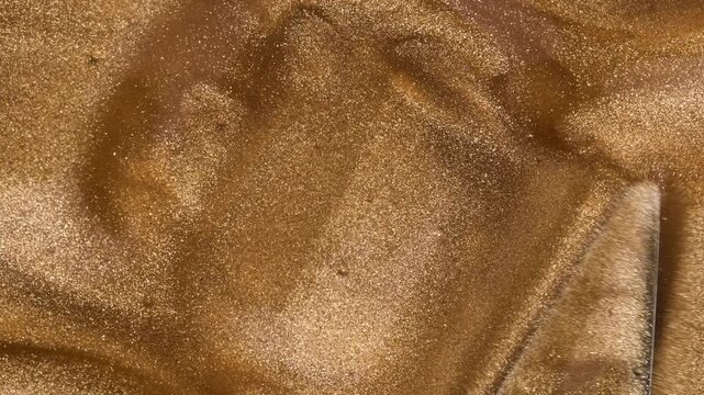 Liquid gold background. Golden brushstroke of liquid gold polish or lip gloss texture, mixing with spatula.