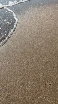 Wave flowing sideways across surface of flat wet brown sand