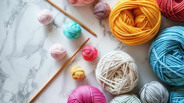 National Craft Month: Overhead flat lay of colorful hand-knitted items, wooden knitting needles, balls of merino wool yarn in pastel colors, crafting tools on white marble surface