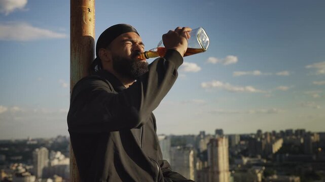 Depressed Black man drinking liquor alone and looking at city from rooftop