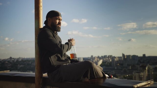 African American man drinking liquor from bottle on rooftop, loneliness