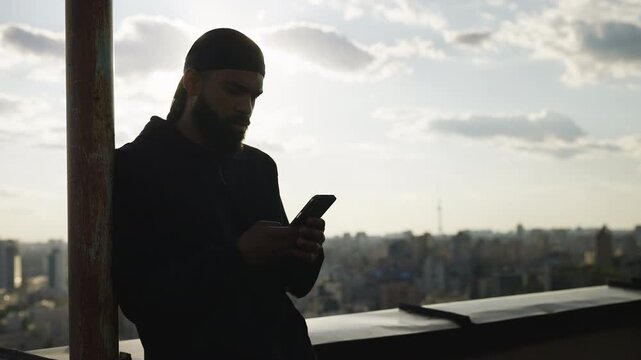 African American male texting on phone on rooftop, waiting to meet someone