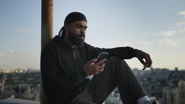 Rebellious young man texting on phone on rooftop while holding bag with weed