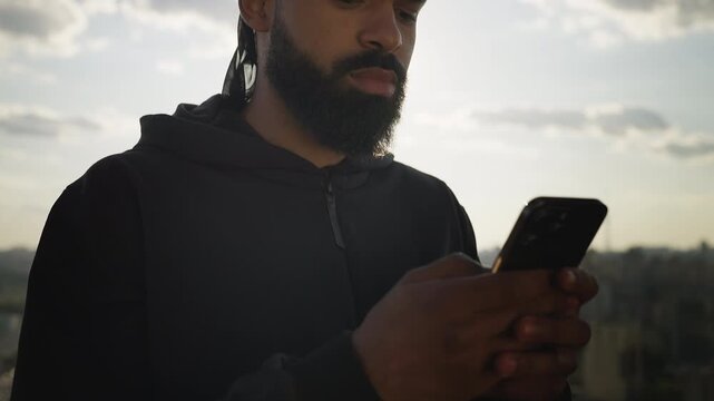 African American male reading message on phone on rooftop, ready for meeting